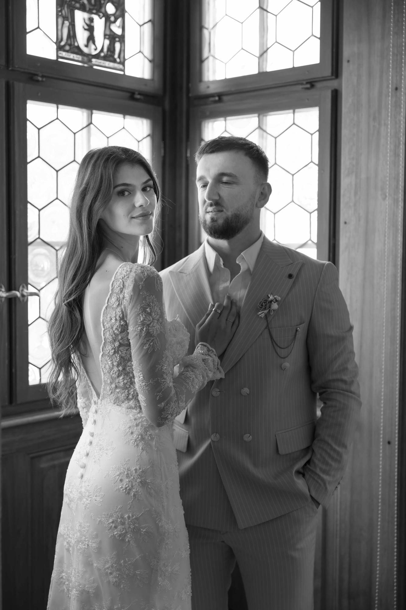 Schwarz-Weiß-Foto eines stilvollen Paares, das vor einem Fenster posiert